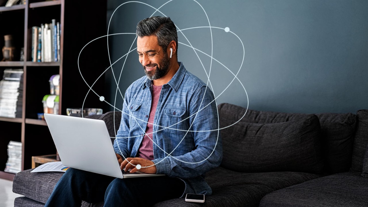 Man with a laptop in his lap while he sits on a couch at home, showcasing remote work style