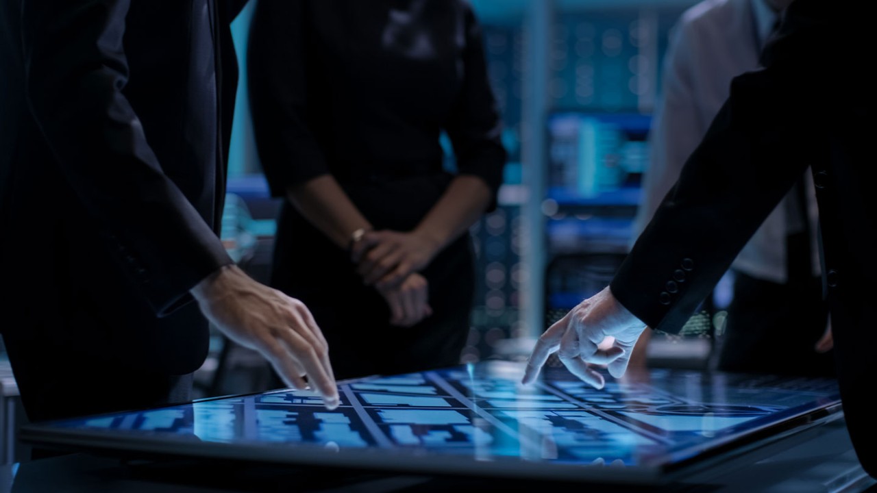 People around a touch screen table pointing out specific areas on the table. 