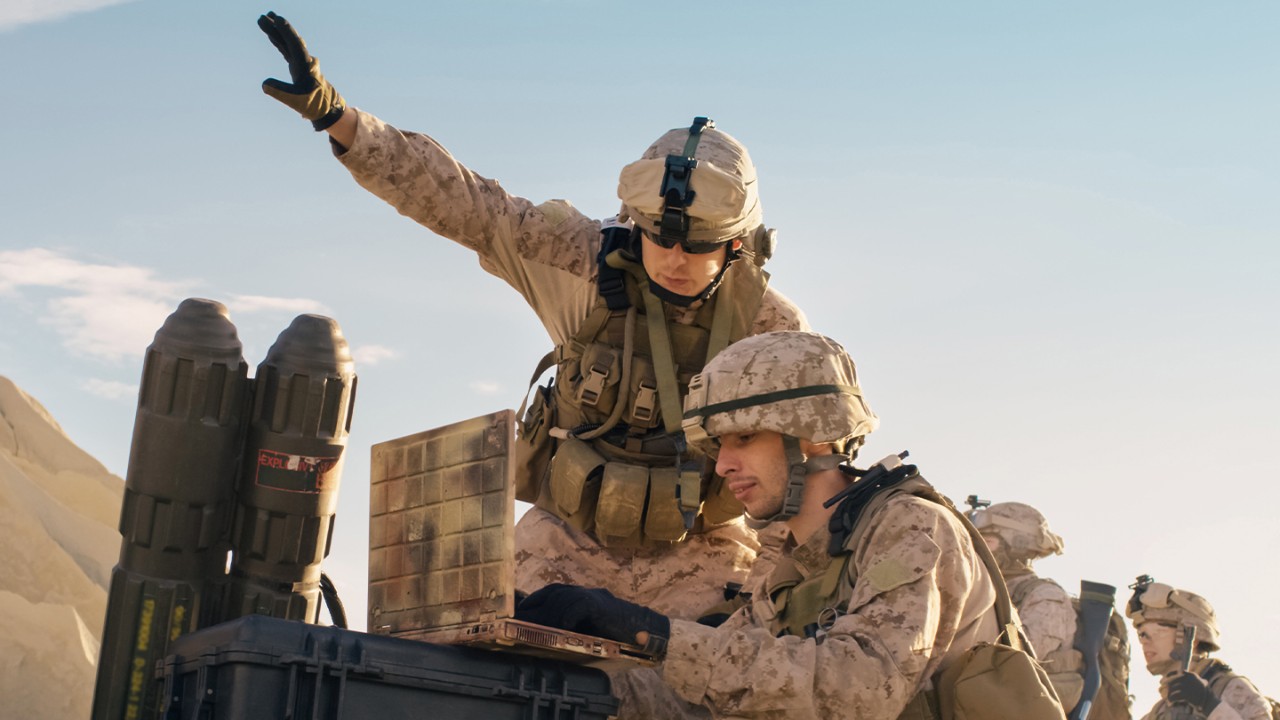 Two soldiers out in the field typing on a laptop.